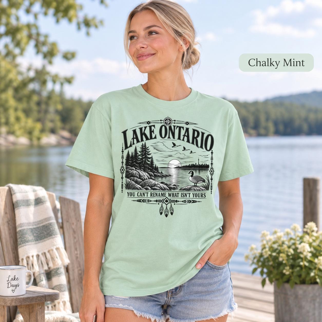 Chalky Mint Comfort Colors Lake Ontario T-shirt featuring a black vintage shoreline design with pine trees, rocky waterfront, Canada goose, Indigenous-inspired geometric details, and the phrase You Can’t Rename What Isn’t Yours.