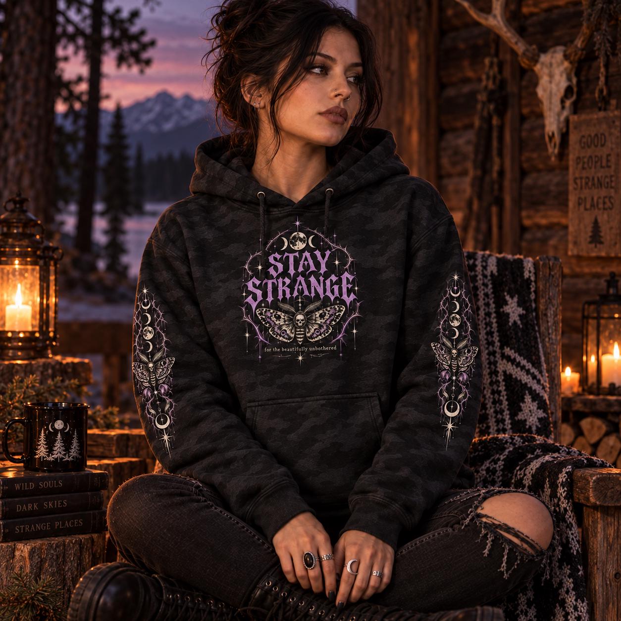 Black camo Stay Strange Social Club heavyweight hoodie featuring purple gothic lettering, death’s-head moth artwork, moon phases, thorn details, and matching celestial sleeve designs.