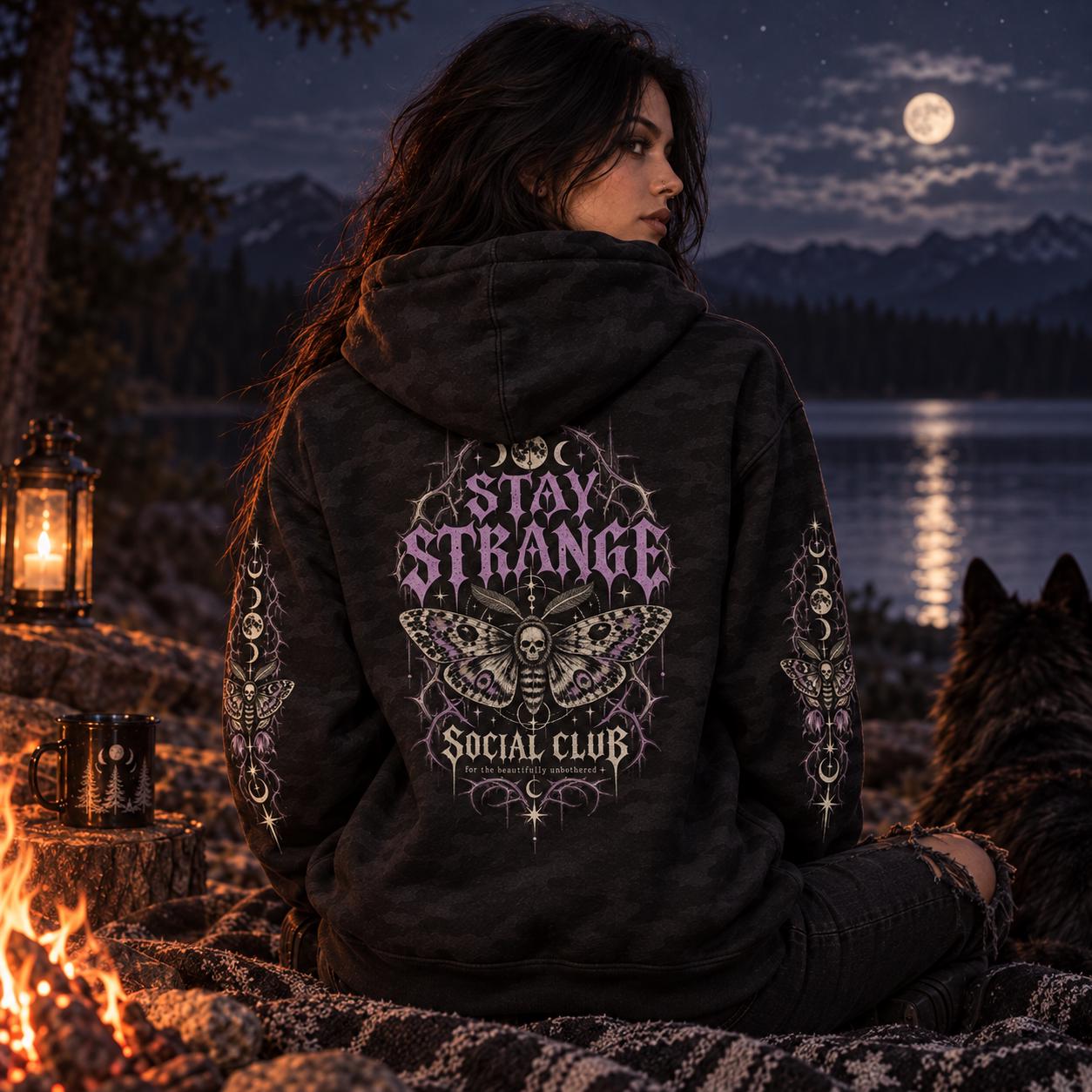 Black camo Stay Strange Social Club heavyweight hoodie featuring purple gothic lettering, death’s-head moth artwork, moon phases, thorn details, and matching celestial sleeve designs.