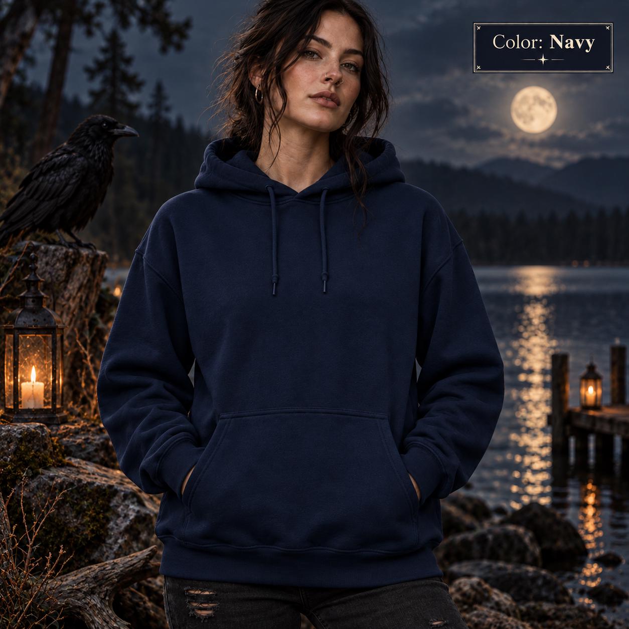 Navy unisex hoodie shown from the front, featuring a large purple raven perched on the back against a glowing violet moon, surrounded by mountains, pine trees, mist, and celestial details.