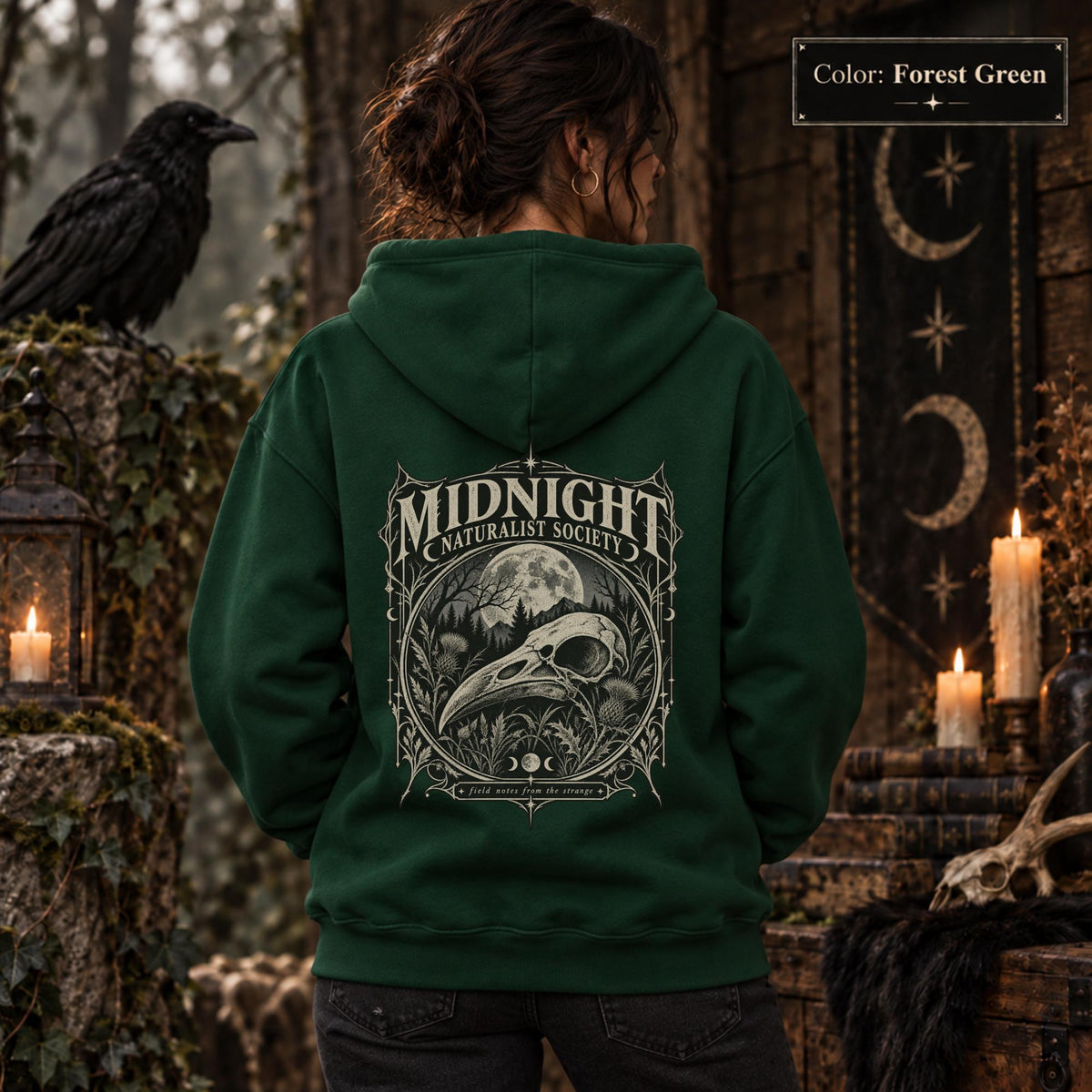 Forest Green unisex hoodie shown from the back with a large Midnight Naturalist Society graphic featuring a bird skull, moon, mountains, forest plants, and vintage gothic botanical details.