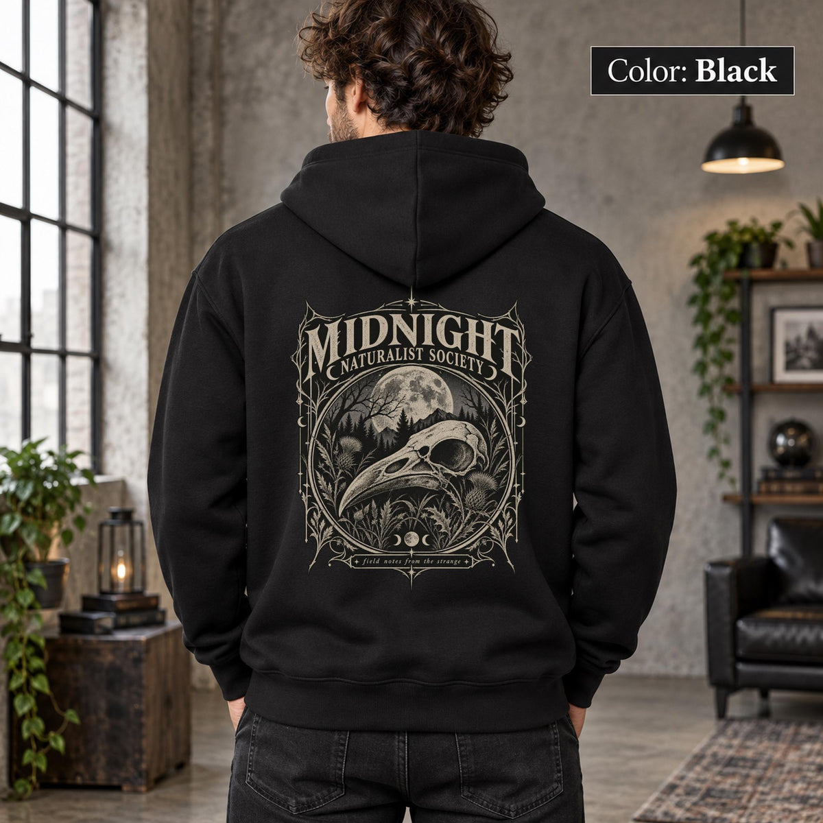 Black unisex hoodie shown from the back with a large Midnight Naturalist Society graphic featuring a bird skull, moon, mountains, forest plants, and vintage gothic botanical details.