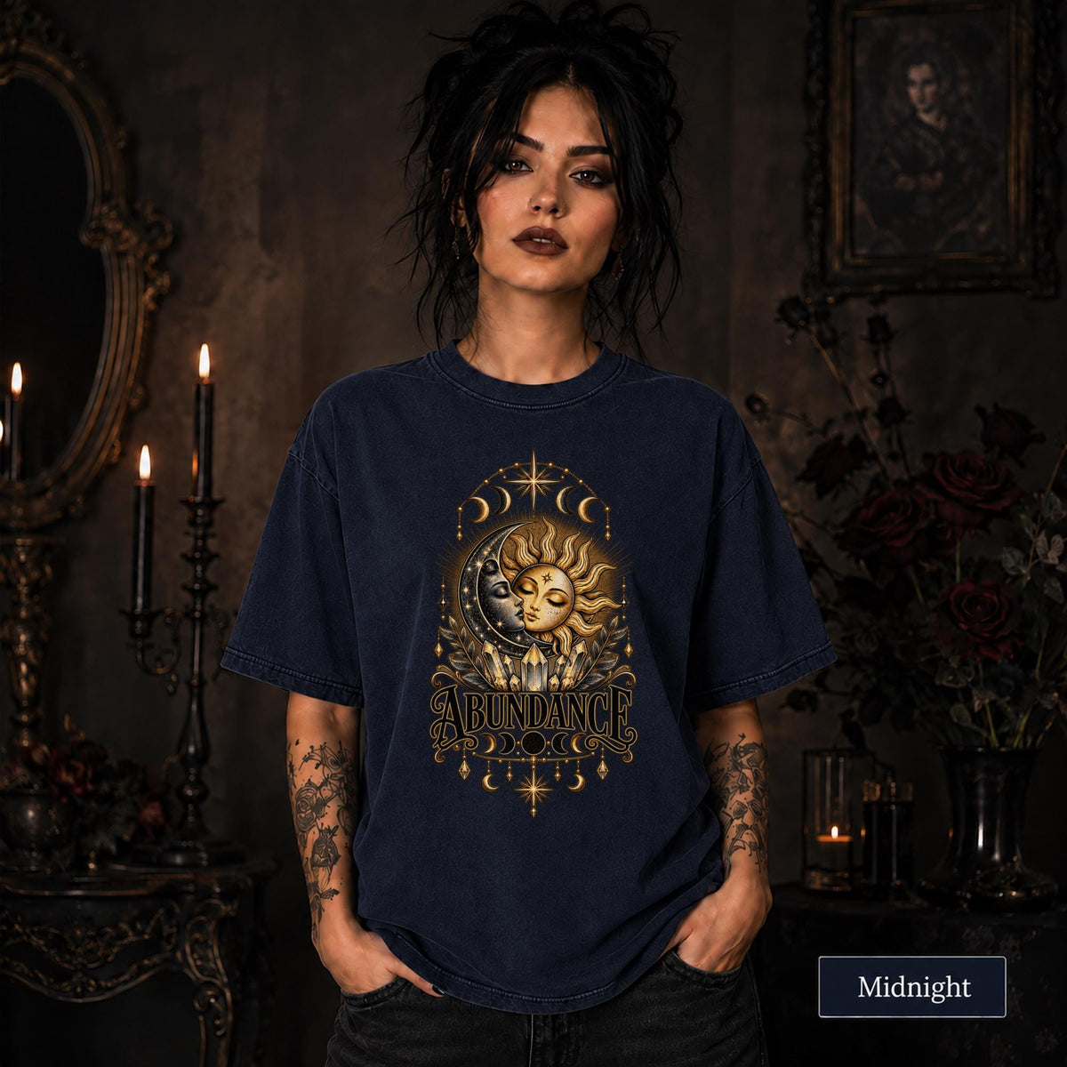 Female model wearing a Midnight Comfort Colors 1717 shirt with a gold celestial Abundance design featuring sun and moon faces, crystals, stars, and moon phases.