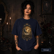 Female model wearing a Midnight Comfort Colors 1717 shirt with a gold celestial Abundance design featuring sun and moon faces, crystals, stars, and moon phases.
