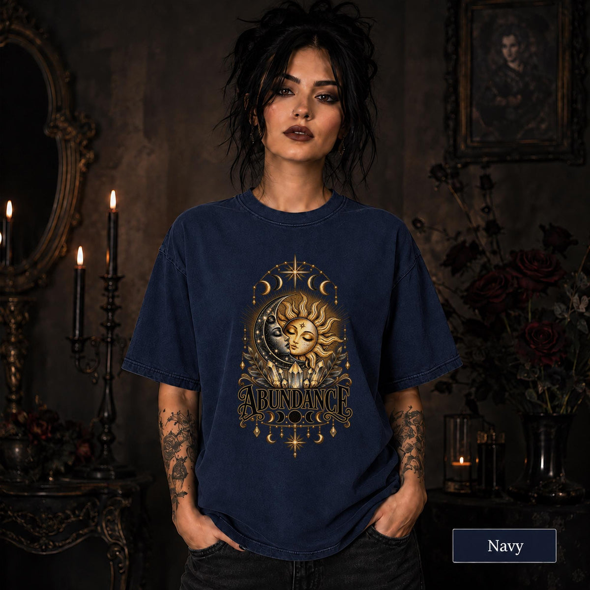Female model wearing a navy Comfort Colors 1717 shirt with a gold celestial Abundance design featuring sun and moon faces, crystals, stars, and moon phases.