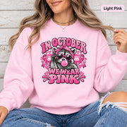 Ash crewneck sweatshirt featuring a retro raccoon in sunglasses with pink ribbons, hearts, bubblegum, and the phrase “In October We Wear Pink.