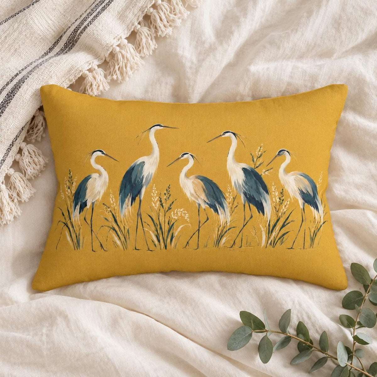 Mustard yellow heron lumbar pillow photographed from above on soft cream linen with neutral woven textiles and eucalyptus greenery.