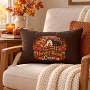 Brown Harvest Haunt Crew lumbar pillow displayed on a cream upholstered chair with chunky knit blanket, pumpkins, autumn leaves, and warm fall decor.