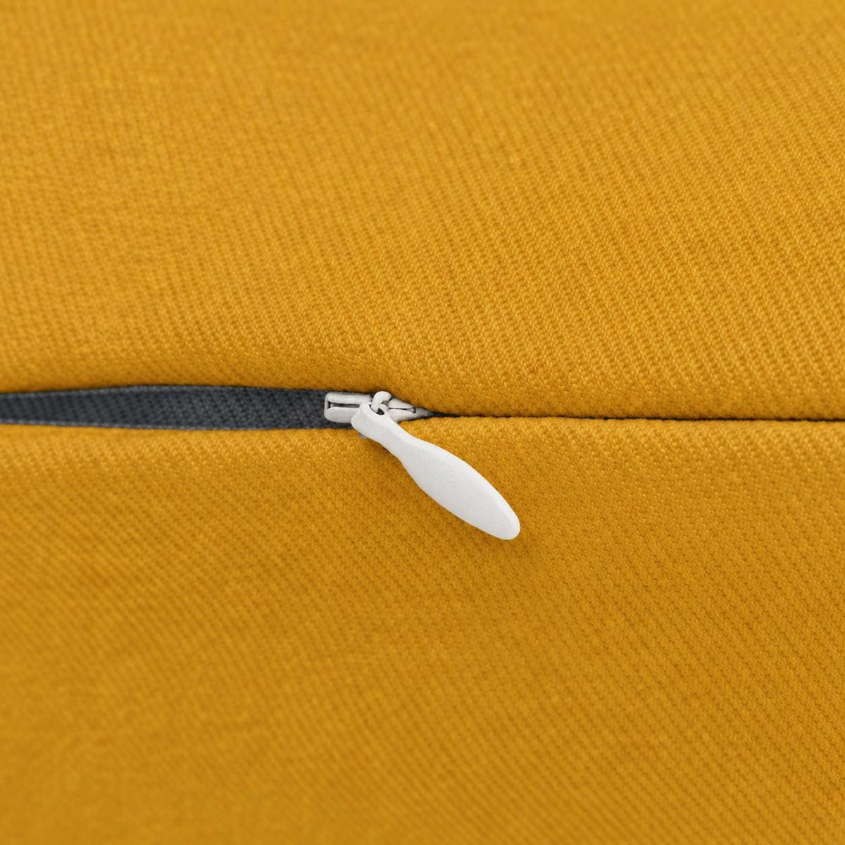 Close-up of mustard yellow pillow fabric showing the concealed zipper, dark zipper tape, and light metal zipper pull.