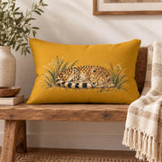 Mustard yellow cheetah lumbar pillow styled on a rustic wooden bench with neutral woven throw, greenery, books, and warm natural decor.