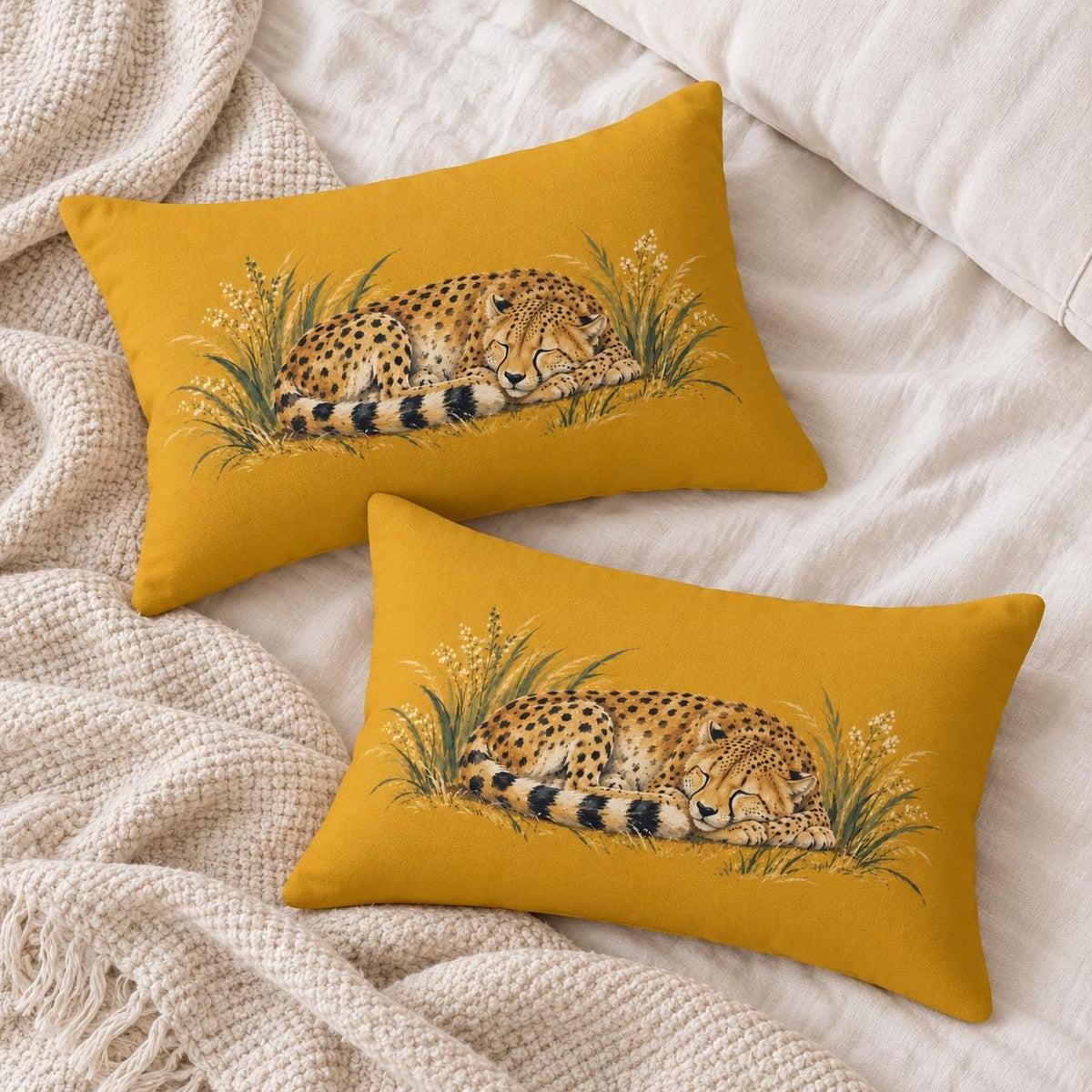 Two matching mustard yellow sleeping cheetah lumbar pillows arranged on soft cream bedding with a textured neutral knit blanket.