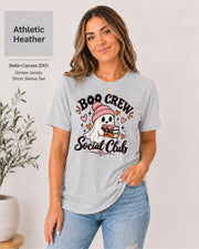 Boo Crew Social Club T-shirt in Athletic Heather featuring a cute ghost in a pink beanie holding books, with hearts, sparkles, and playful Halloween lettering.