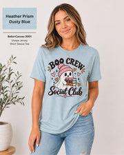 Boo Crew Social Club T-shirt in Heather Prism Dusty Blue featuring a cute ghost in a pink beanie holding books, with hearts, sparkles, and playful Halloween lettering.