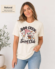 Boo Crew Social Club T-shirt in Natural featuring a cute ghost in a pink beanie holding books, with hearts, sparkles, and playful Halloween lettering.