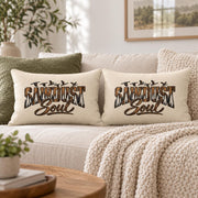 Two matching Sawdust Soul lumbar pillows styled together on a cream sofa with olive accent pillow, chunky knit blanket, and neutral woodland home decor.