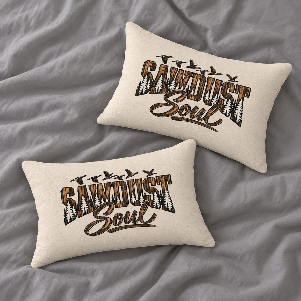 Two matching cream Sawdust Soul lumbar pillows arranged on soft gray bedding, showing the rustic woodland typography design from different angles.