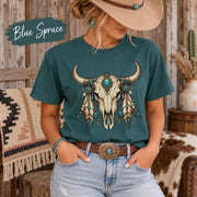 Blue Spruce tee displaying the Western bull skull design with layered feathers, jewelry, and earthy desert colors.