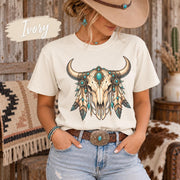 Ivory tee showcasing the bull skull graphic with teal stones, feathers, beads, and soft Southwestern tones.