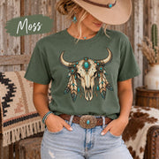 Moss tee displaying the decorative longhorn skull artwork with feathers, beads, and ranch-inspired colors.