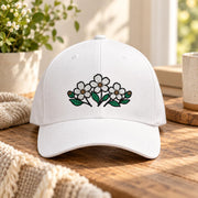 White structured Flexfit cap featuring an embroidered cluster of small white flowers with green leaves centered on the front.