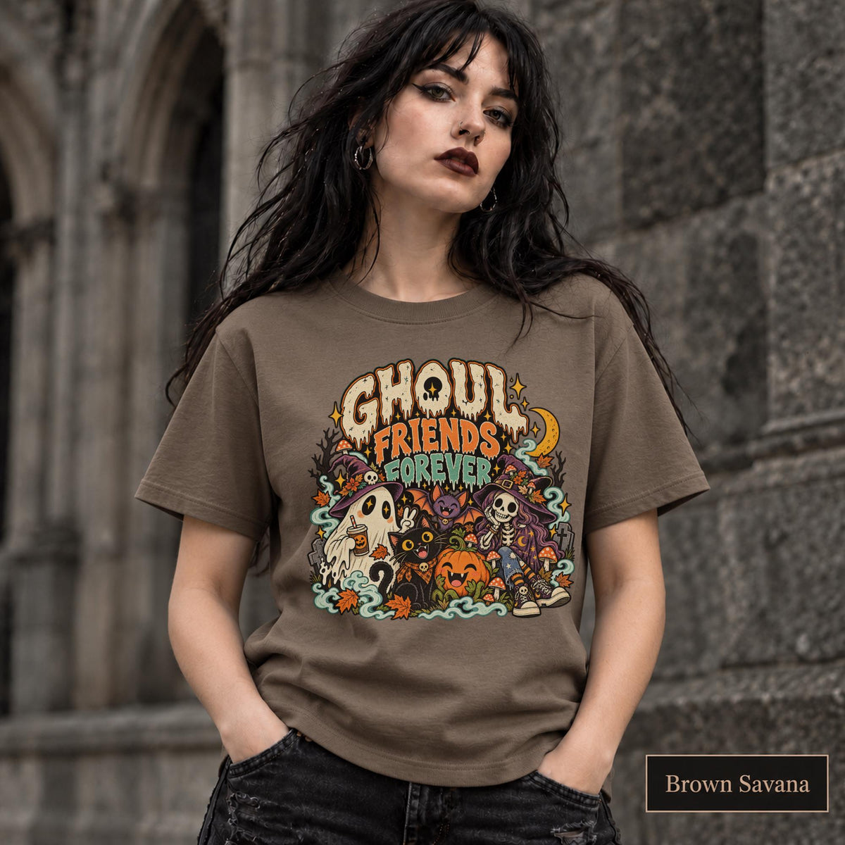 Brown Savana unisex T-shirt featuring a colorful “Ghoul Friends Forever” Halloween graphic with a ghost, black cat, pumpkin, witchy skeleton, bats, mushrooms, crescent moon, and autumn accents.