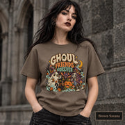 Brown Savana unisex T-shirt featuring a colorful “Ghoul Friends Forever” Halloween graphic with a ghost, black cat, pumpkin, witchy skeleton, bats, mushrooms, crescent moon, and autumn accents.
