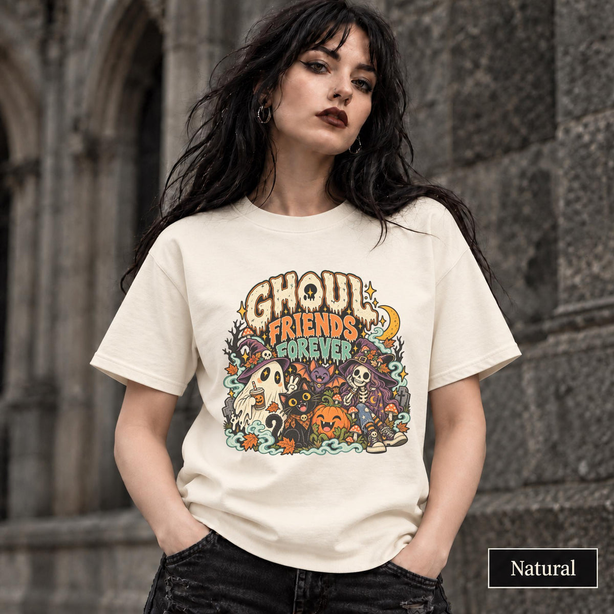 Natural unisex T-shirt featuring a colorful “Ghoul Friends Forever” Halloween graphic with a ghost, black cat, pumpkin, witchy skeleton, bats, mushrooms, crescent moon, and autumn accents.