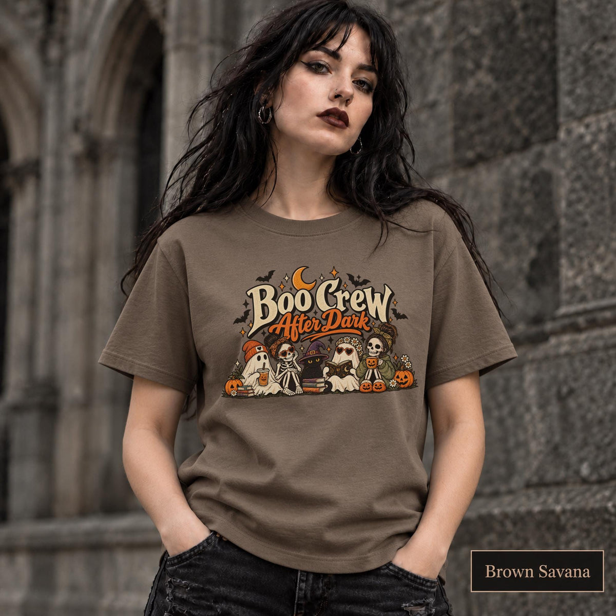 Brown Savana unisex T-shirt featuring a “Boo Crew After Dark” Halloween design with ghosts, skeletons, pumpkins, books, bats, drinks, and a crescent moon in retro orange and cream tones.