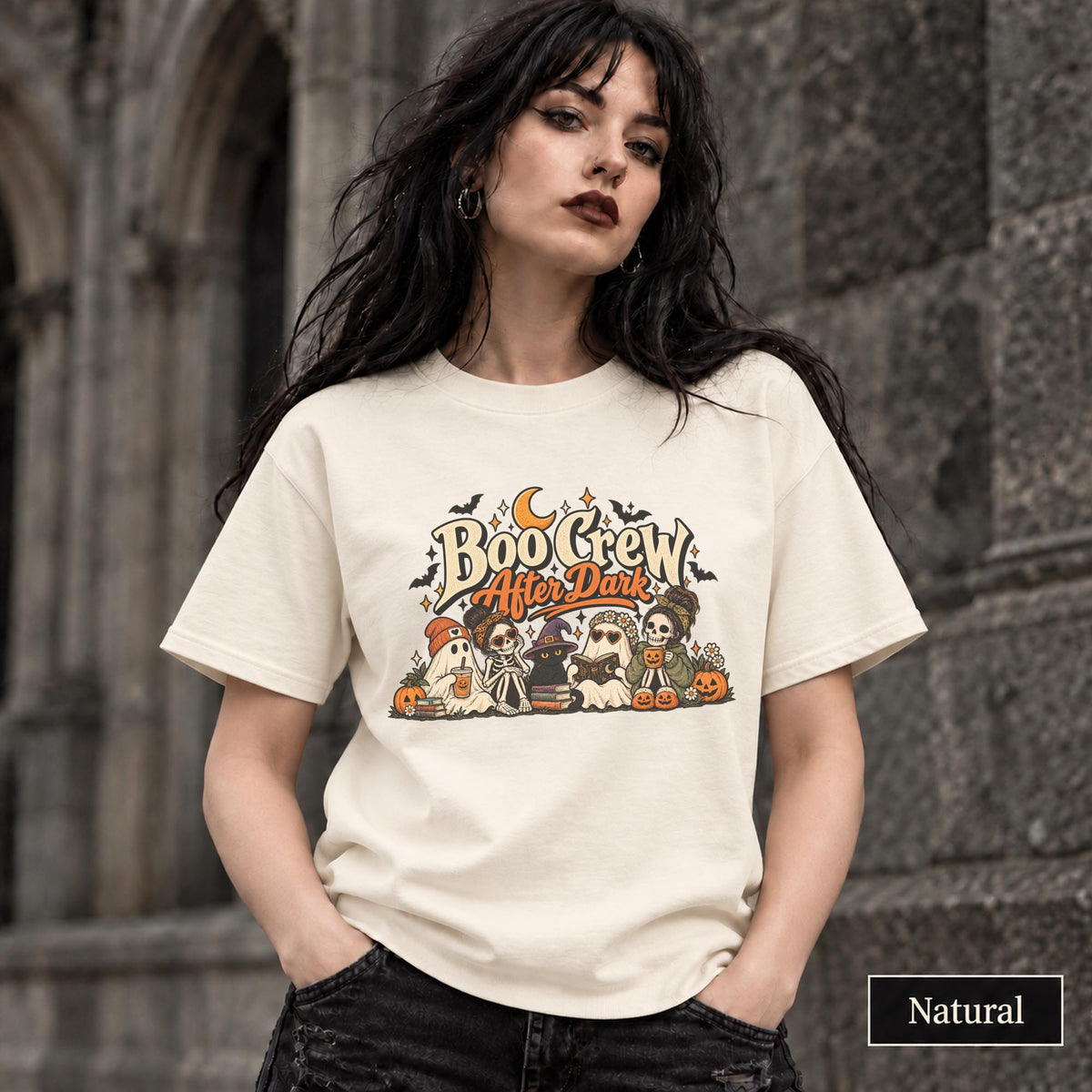 Natural unisex T-shirt featuring a “Boo Crew After Dark” Halloween design with ghosts, skeletons, pumpkins, books, bats, drinks, and a crescent moon in retro orange and cream tones.