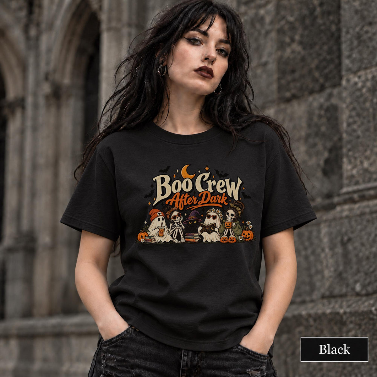 Black unisex T-shirt featuring a “Boo Crew After Dark” Halloween design with ghosts, skeletons, pumpkins, books, bats, drinks, and a crescent moon in retro orange and cream tones.