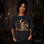 Midnight unisex T-shirt featuring a gothic fantasy scene with a unicorn, owls, raven, crescent moon, mushrooms, candles, flowers, and twisted woodland branches.