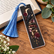 Dark academia raven bookmark with blue tassel displayed on an open journal with crescent moon, books, roses and crystal artwork.