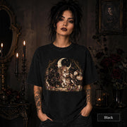 Black unisex T-shirt featuring a gothic fantasy scene with a unicorn, owls, raven, crescent moon, mushrooms, candles, flowers, and twisted woodland branches.