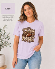 Lilac Bella+Canvas 3001 unisex T-shirt featuring a customizable vintage football graphic with bold “Team Name” lettering, leopard-print bow, stars, and distressed varsity details.