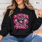 Black crewneck sweatshirt with a bright pink raccoon awareness design, ribbon symbols, hearts, and bold supportive wording.