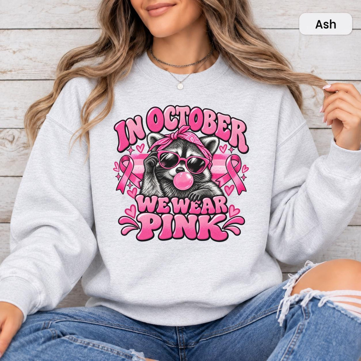 Ash sweatshirt mockup with a funny raccoon, pink bubblegum, sunglasses, and “In October We Wear Pink” awareness phrase.