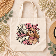 Cream canvas tote bag mockup showing the funny dog lover PNG artwork with playful pink and cream lettering, styled with neutral boho accessories.