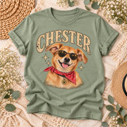 Styled sage green shirt flat lay featuring Chester's personalized dog portrait with distressed name typography, a golden dog illustration wearing sunglasses, and coordinated botanical decorations.