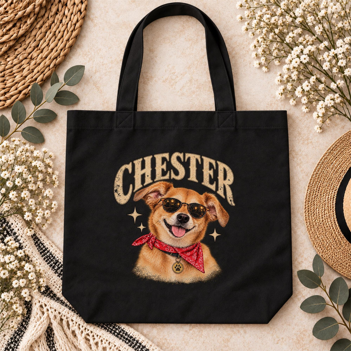 Black canvas tote bag mockup featuring the custom Chester dog portrait design with retro name lettering, sunglasses, red bandana and warm vintage colors, surrounded by neutral decorative accessories.