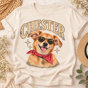 Cream T-shirt flat lay featuring a personalized Chester dog portrait with large vintage lettering, a happy golden dog wearing sunglasses and a red bandana, styled with neutral boho accessories.