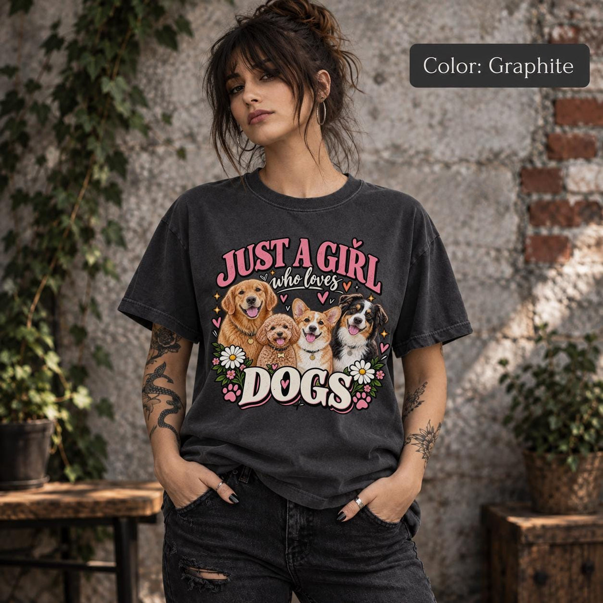Lifestyle mockup of a woman wearing a graphite T-shirt displaying vintage-inspired Just a Girl Who Loves Dogs artwork with four dogs, pink hearts and floral accents.