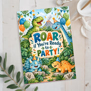 Dinosaur birthday party invitation featuring three cheerful cartoon dinosaurs, colorful balloons, tropical jungle leaves and Roar Some Fun lettering, displayed in a styled tabletop mockup.