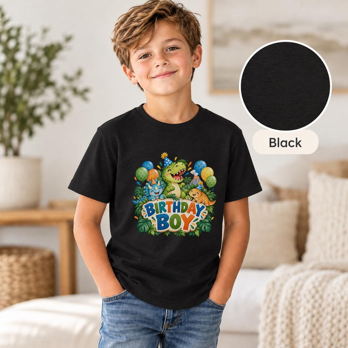 Young boy modeling a black dinosaur birthday shirt featuring green, blue and orange cartoon dinosaurs, tropical jungle leaves, balloons and playful Birthday Boy typography.