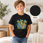 Young boy modeling a black dinosaur birthday shirt featuring green, blue and orange cartoon dinosaurs, tropical jungle leaves, balloons and playful Birthday Boy typography.