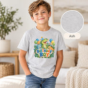 Smiling boy wearing an ash grey dinosaur party T-shirt featuring a cheerful green dinosaur, blue triceratops, orange stegosaurus and colorful Birthday Boy artwork.