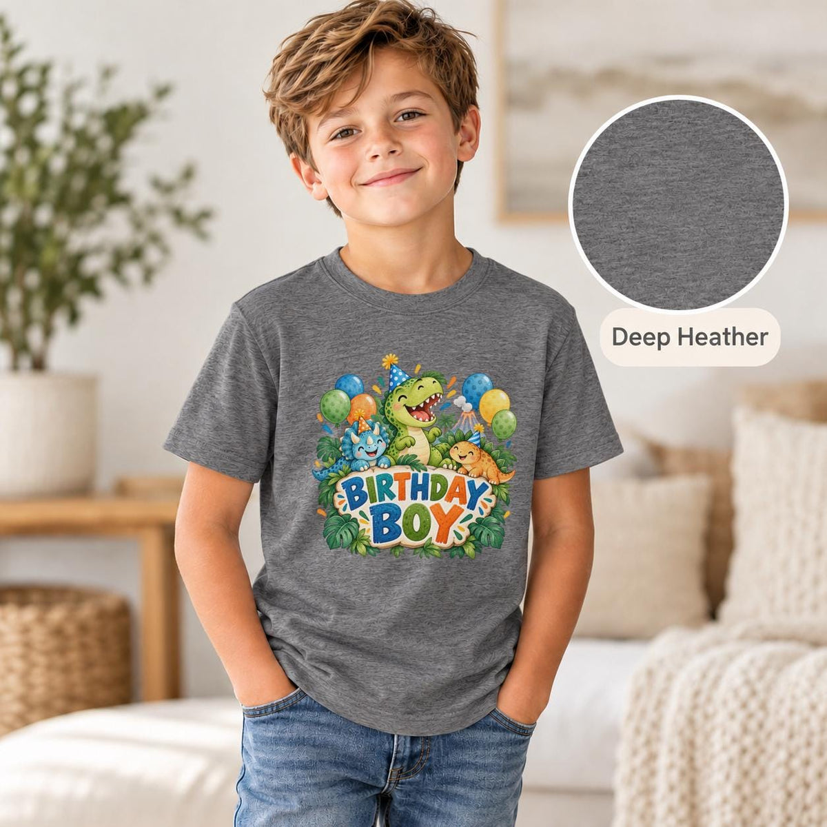 Young boy modeling a deep heather grey dinosaur birthday shirt decorated with three smiling prehistoric animals, party balloons and colorful jungle-inspired details.