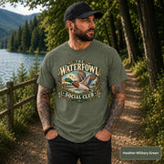 Heather Military Green tee displaying the flying mallard graphic with marshland scenery and earthy badge-style artwork.