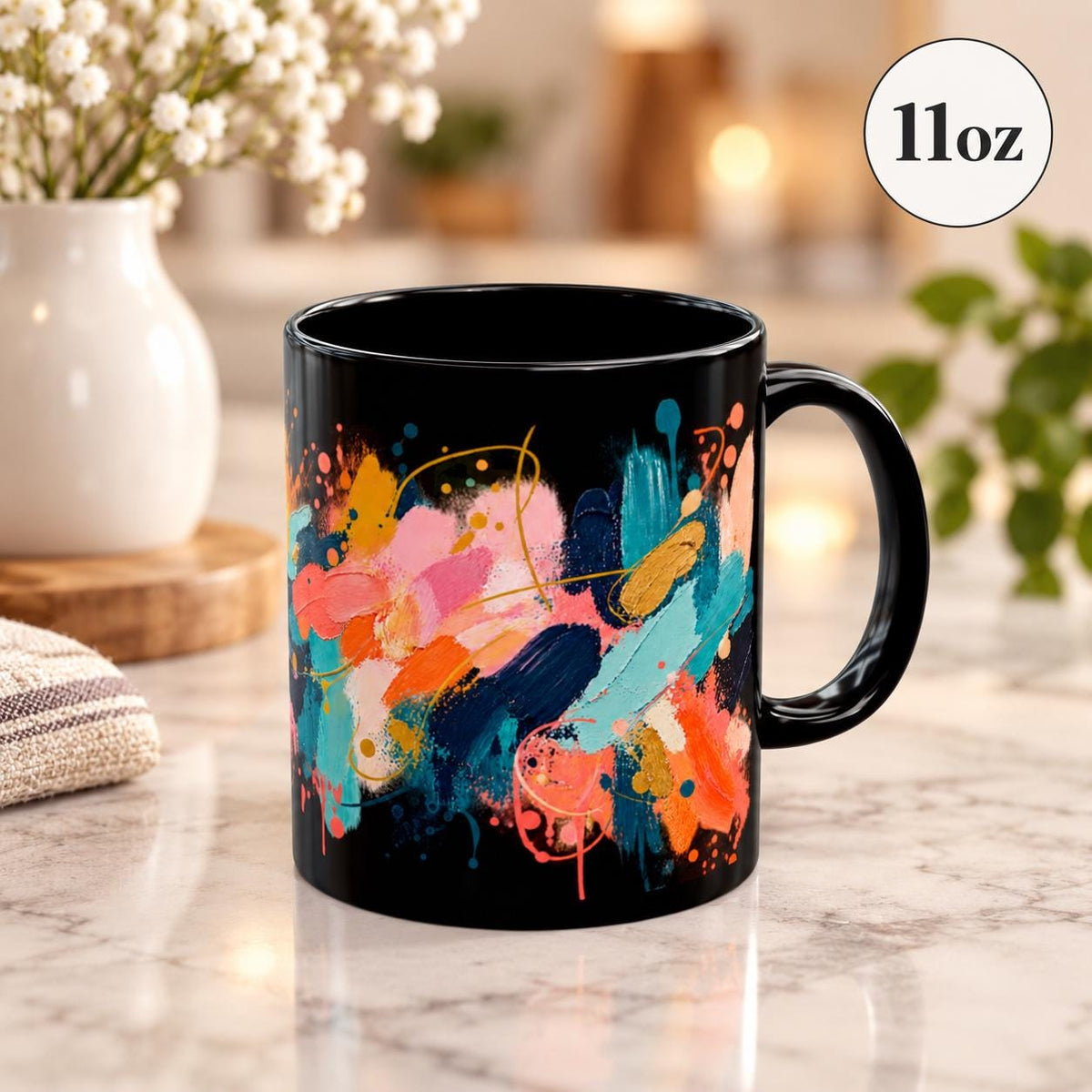 Black ceramic mug featuring bold abstract brushstrokes in coral, turquoise, orange, cream, pink, and teal on a bright neutral tabletop.