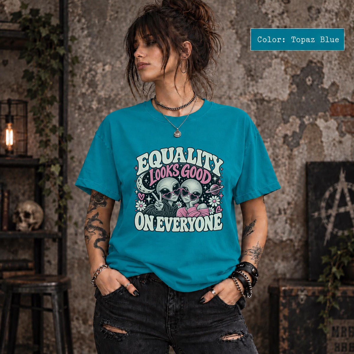 Topaz Blue Comfort Colors shirt featuring the equality message with two alien characters, hearts, flowers, and celestial elements.