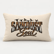 Cream rectangular Sawdust Soul lumbar pillow shown on a clean light background with bold rustic brown and black lettering, pine tree silhouettes, and flying birds.